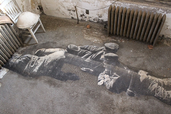 A life-sized black-and-white photo plastered onto a concrete floor. Three young boys are lying on the ground in the photo. 