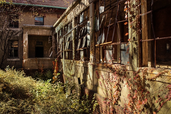View of abandoned hospital from outside. Windows are broken and vines grow over the building.