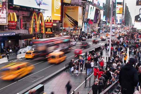 A view from the Red Steps in Times Square, looking down onto the street. Taxis, a bus, and cars are going by in a blur. McDonald's is in the background. 