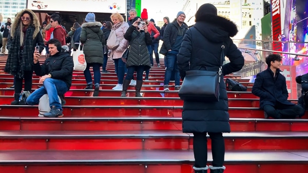The Red Steps in Times Square. Photo is taken from the bottom of the steps, looking up. About 15 people are in the photo, spread around on the steps taking photos, sitting down, etc.