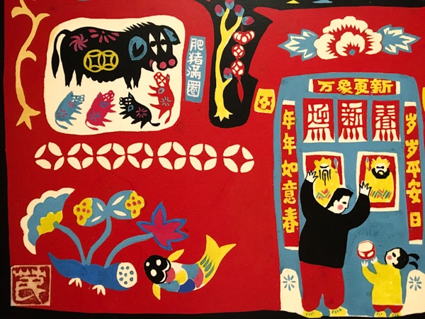 Clockwise from top left: a yellow branch, a black pig with four baby pigs underneath her, a yellow tree, a blue and white flower, a father and daughter standing in front of a wall, a fish, a plant. The background is entirely in red. The elements mentioned are in various colors, mostly black, blue, and yellow. 