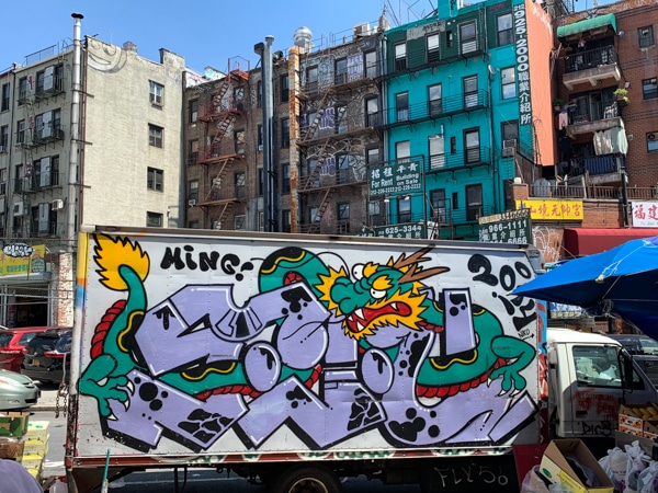 A delivery truck decorated with graffiti in Chinatown. Apartment buildings rise up in the background.