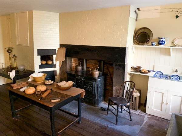 Kitchen inside Merchant's House Museum. It is staged to appear that it's in use: fake loaves of bread sit on the wooden table, a fake rat sits next to a chair to illustrate the rodent problem. 