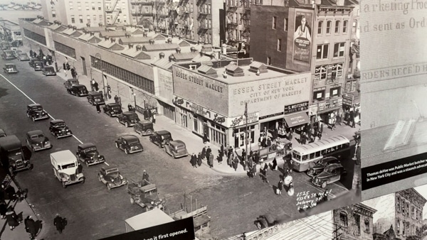 An old, black and white photo of Essex Street Market. The photo is an aerial shot taken of the corner of Essex and Delancey Streets. 