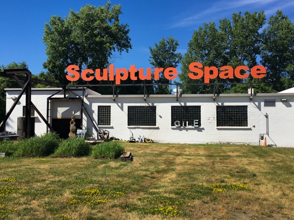 Exterior photo of Sculpture Space. The facility's name is shown in bright orange letters on the front of the building.