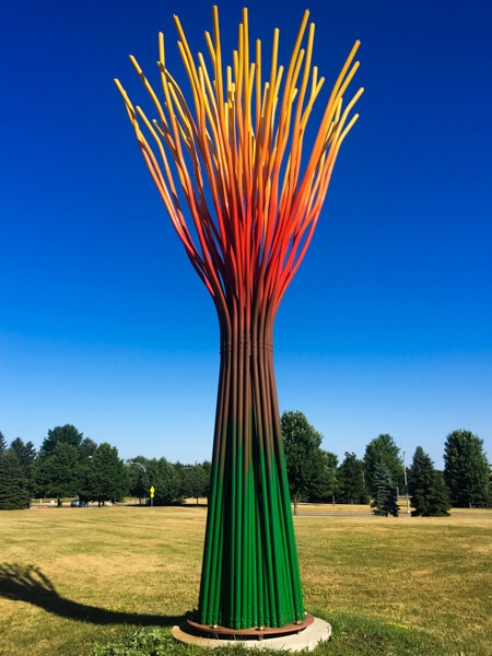 Large outdoor sculpture called Persephone. Somewhat resembles a tree without leaves. Trunk is green, and branches are red and yellow.