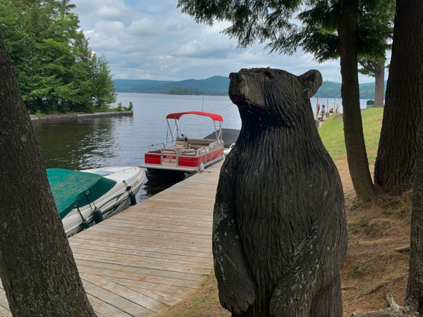 Channel between Fourth and Fifth Lakes. Two boats are docked against a boardwalk. A carved wooden bear is on a small hill next to the boardwalk.