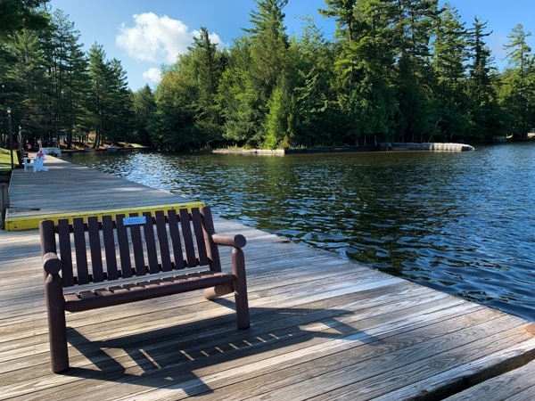 Photo is taken from the end of the dock at Fourth Lake. A brown wooden bench sits on the dock.