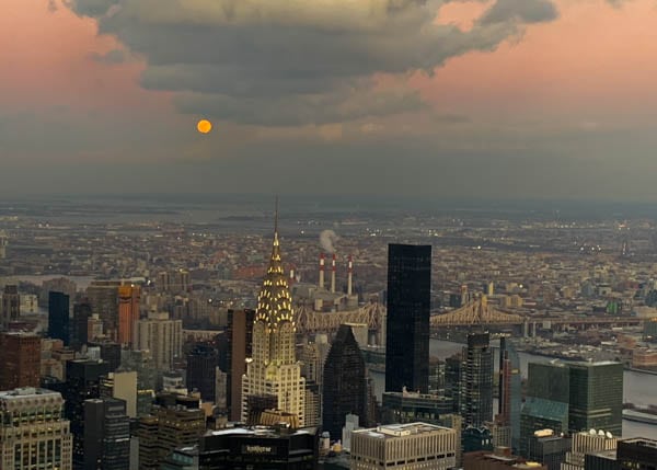 View from the Empire State Building: the moon is rising over the Chrysler Building.