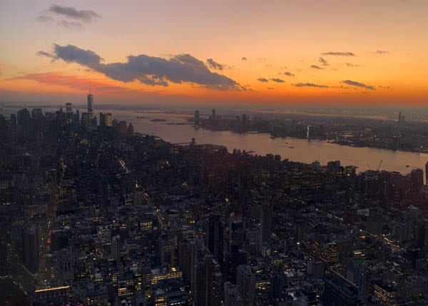 View from the Empire State Building looking south toward One World Trade. The sunset is orange and red.