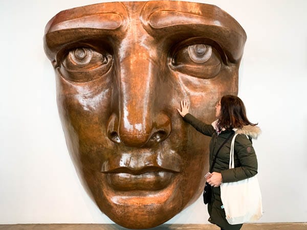 A large copper model of the Statue of Liberty's face. The author is standing in front of it touching the model's face.