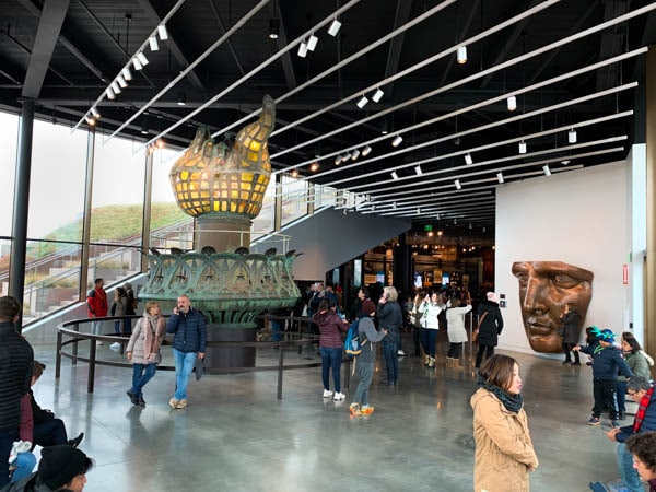 Another shot of the old torch, this time taken from further away. The copper model face can also be seen nearby. Several museum-goers are also in the photo.