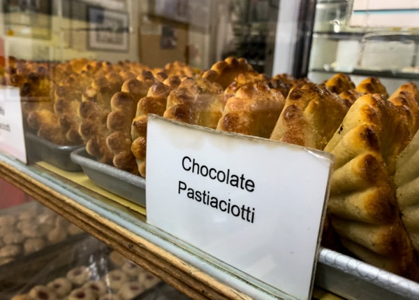 A row of Italian, custard-filled pastries, displayed on a pastry shelf behind glass