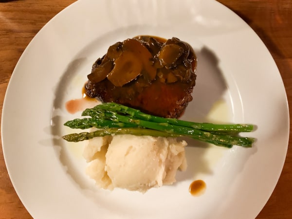 Filet mignon, a scoop of mashed potatoes, and asparagus on a plain white plate. 