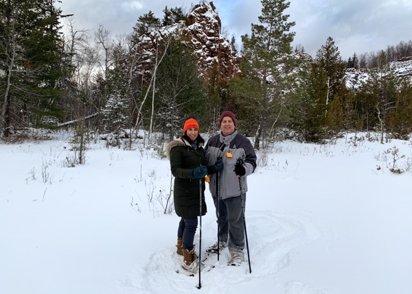 A man and a woman in a snowy field and wearing snowshoes. 