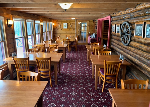 Restaurant with two rows of tables. The walls are made of long natural logs, like in a log cabin. 