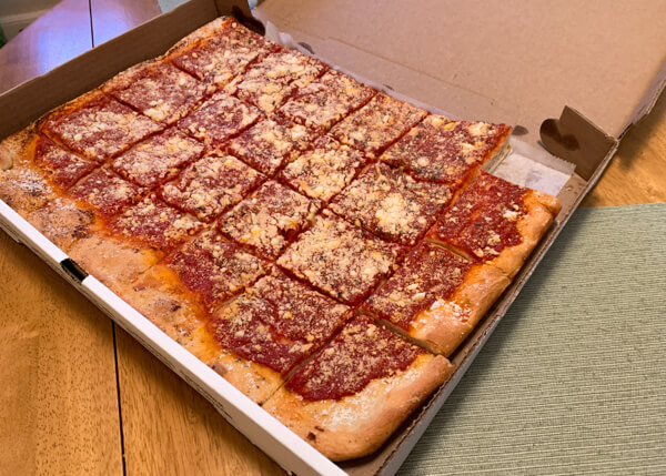Whole tomato pie inside a pizza box with one piece missing.