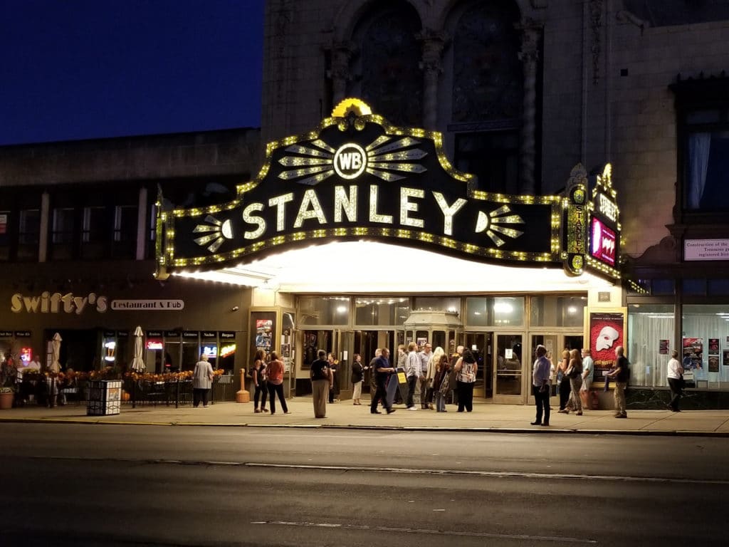 Stanley Theatre in Utica, NY at night with a small crowd of people in front of the theater.