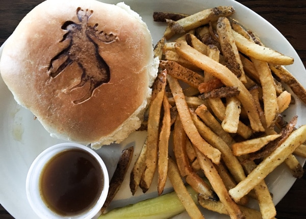 Hamburger and French fries, with a pickle and dipping sauce on the side. An image of a moose is branded onto the hamburger bun.