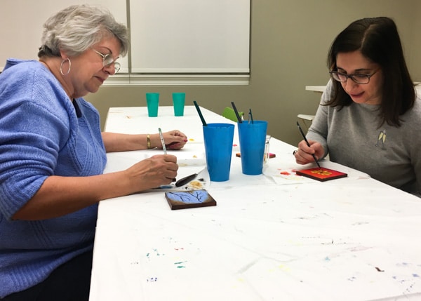 Two women painting on small coaster-sized canvases.