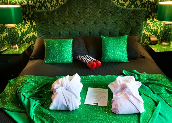 King-sized bed with a dark green velvet headboard, emerald green pillows and throw, and a pillow that looks like the Wicked Witch of the East's legs. 
