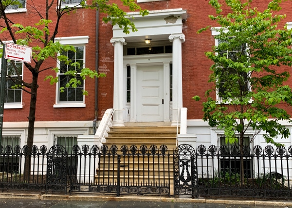 Exterior of a brick rowhouse. Steps lead up to the porch, which is framed by two white pillars. 