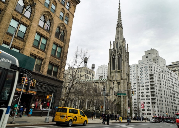 The spire of Grace Church in New York City. A yellow cab is parked on the street.