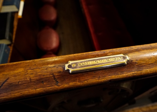 The railing of a wooden church pew. The name "Schermerhorn" is engraved on a small gold name plate. 