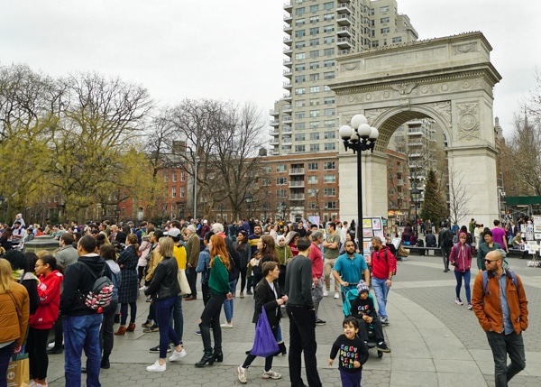 A crowd of people in Washington Square Park. The arch is in the background. 