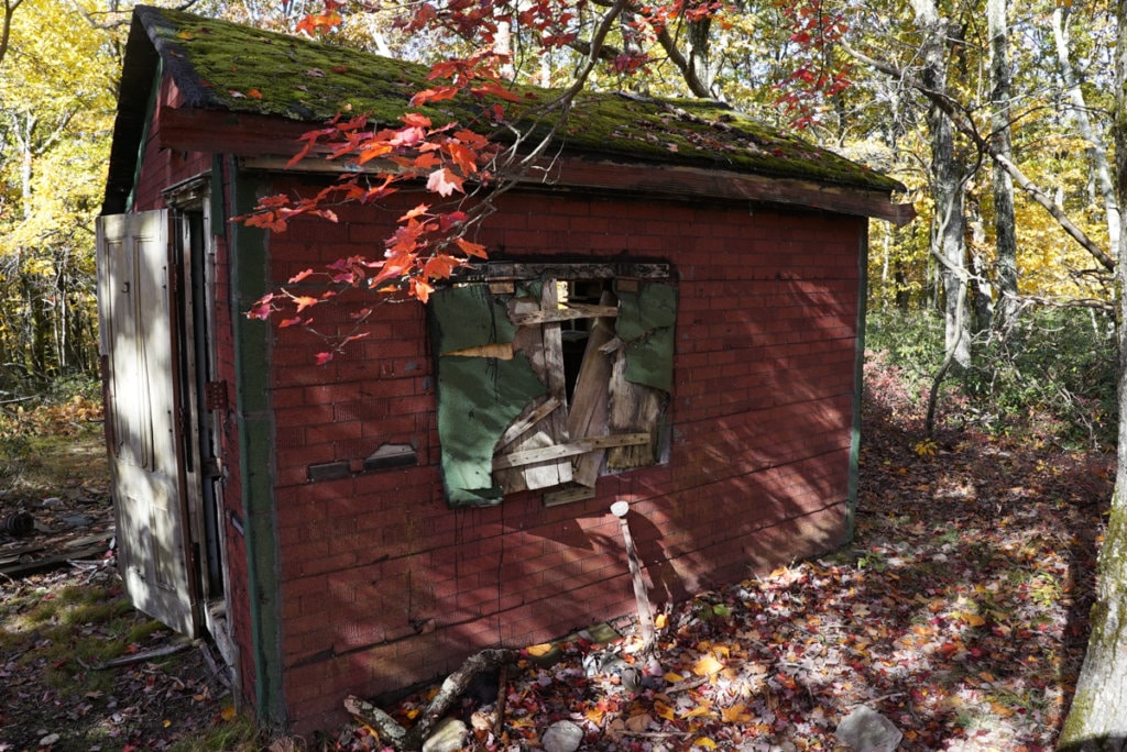 A small, dilapidated, red cabin with one boarded-up window.