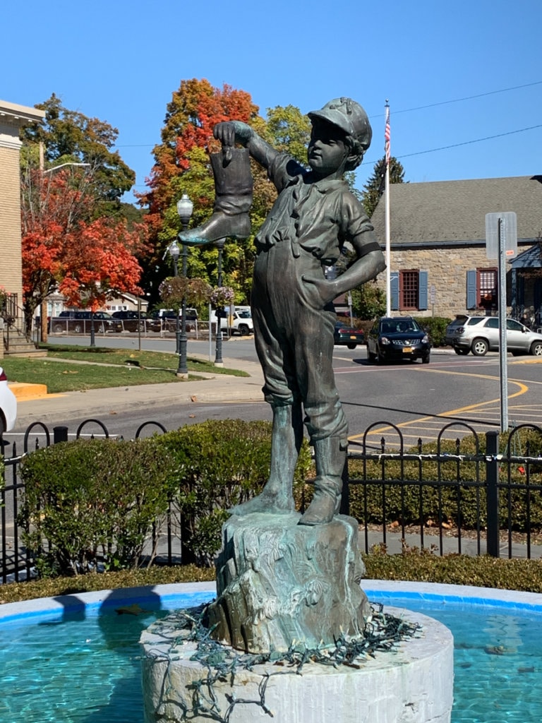 An old fountain with a statue in the middle depicting a young boy holding up and looking at a boot. 