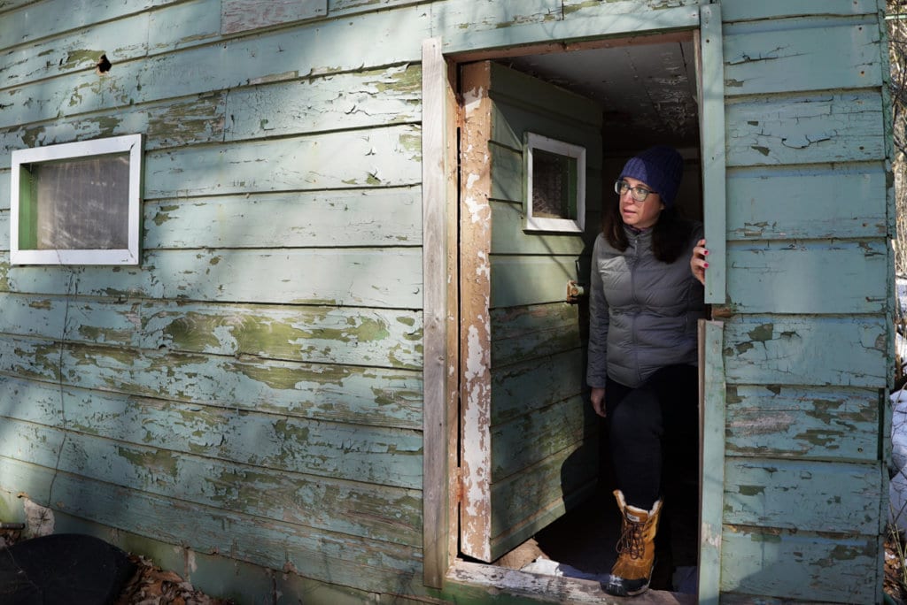 Woman standing in the doorway of a dilapidated green building.