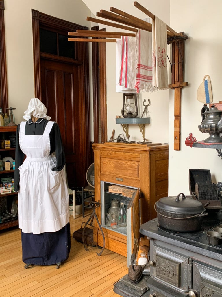 A Victorian-era kitchen, with a mannequin dressed in a black-and-white maid's outfit.