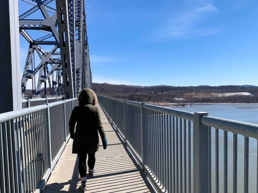 Back view of a person walking on a bridge that crosses the Hudson River.