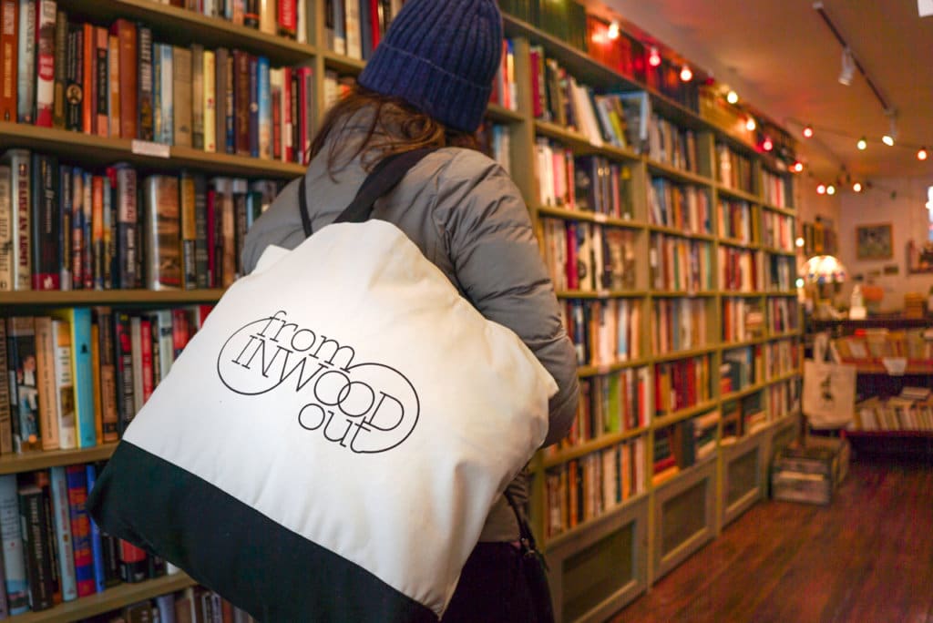 Person from behind looking at books in a bookstore. Tote bag that says, "from Inwood out."