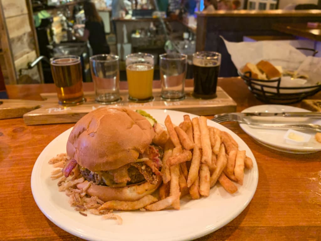 Hamburger and French fries with a beer flight behind it.