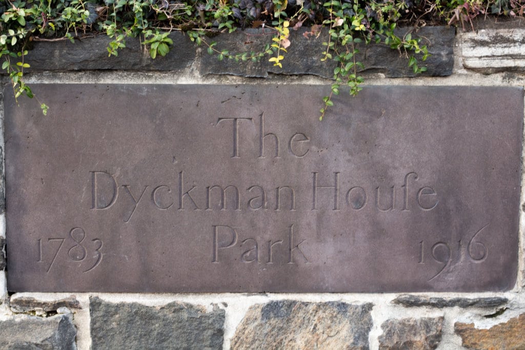 Words etched into a concrete slab outside a farmhouse. It says, "The Dyckman Houfe Park 1783 - 1916"