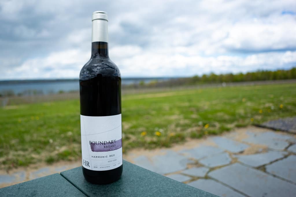 Bottle of red wine on a table outside with lake in the background. 