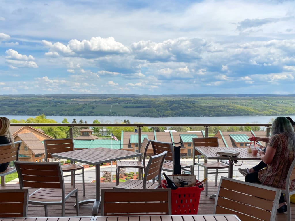 Deck with several sets of table and chairs, looking out over Seneca Lake. 