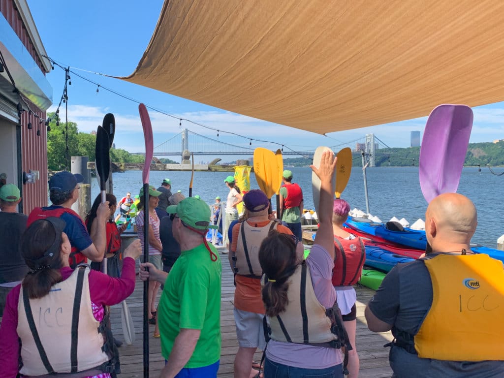 Several people standing on a dock holding kayak paddles. 