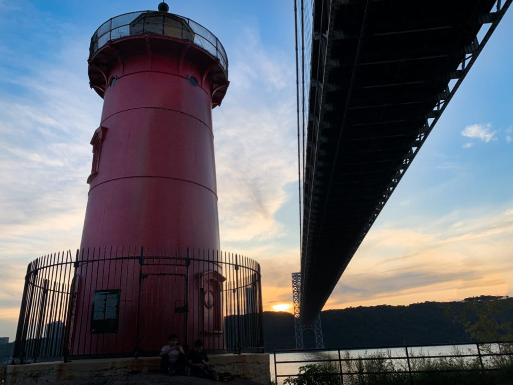 Red lighthouse with the George Washington Bridge spanning the river next to it.