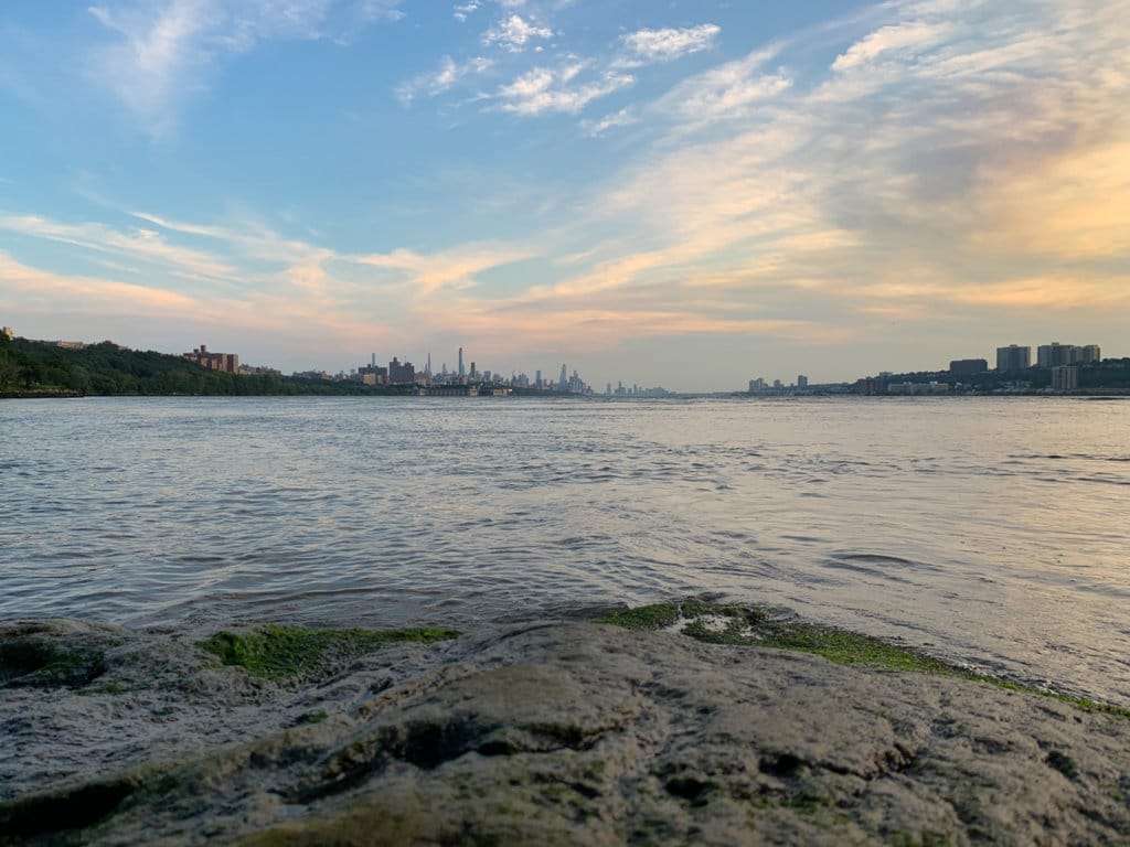 Rocky coast of the Hudson River with the Manhattan skyline in the distance. 