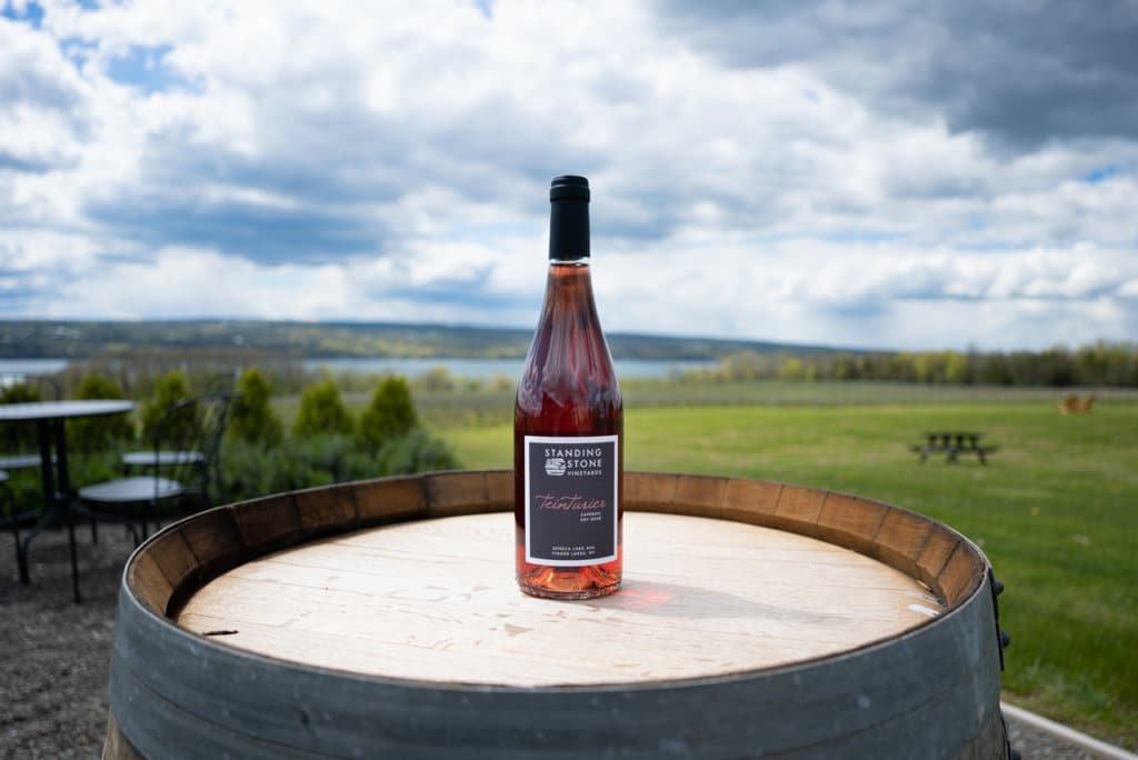 Bottle of rose wine sitting on top of a barrel with the lake in the distance. 