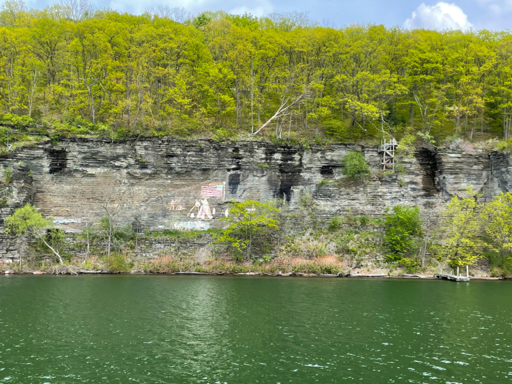 A flat cliff rising out of the lake with images painted on. The only visible image is the American flag.