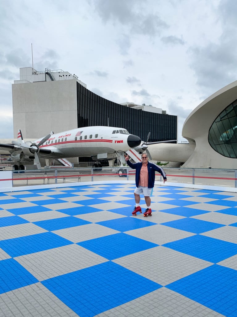 Man rolling skating on blue and white checkered rink. Small propeller plane is behind him. 