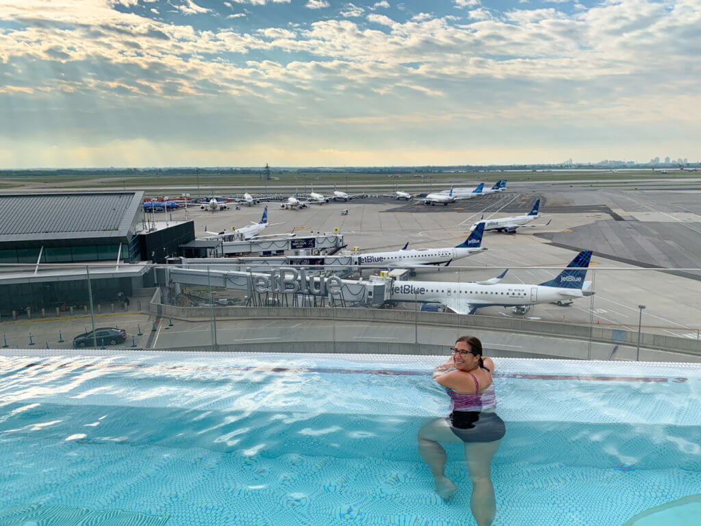 Woman in an infinity rooftop pool with a view of an airport runway in the background.