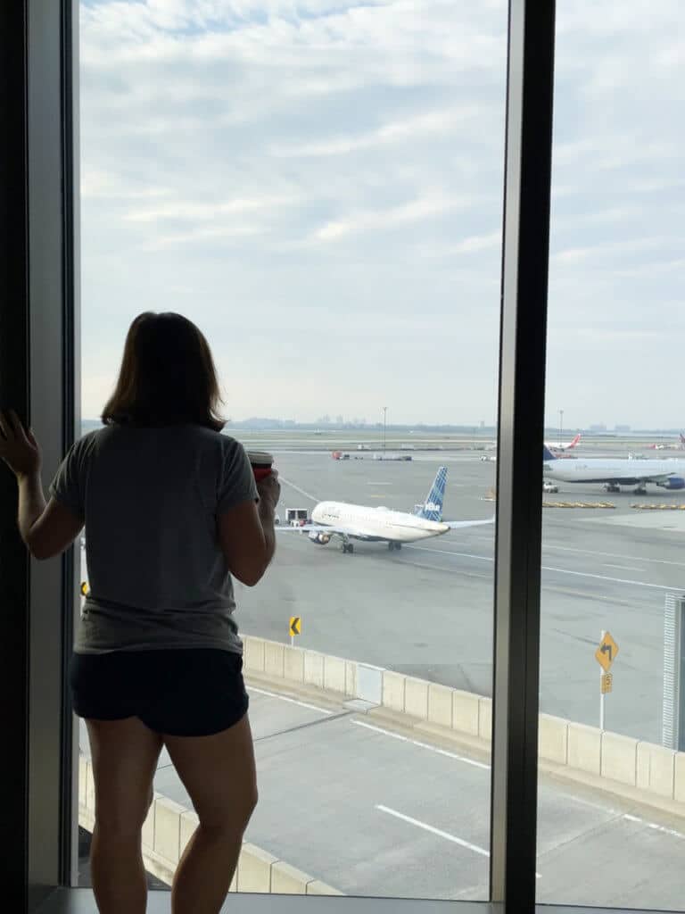 Woman looking out hotel room floor-to-ceiling window onto airport runway.