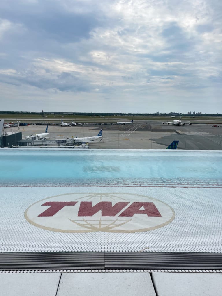 Rooftop infinity pool with a TWA logo on the pool floor. Airport runway in background.