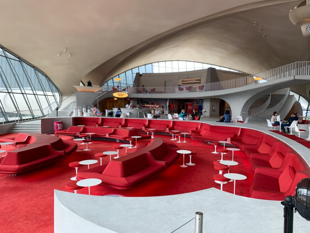Airport lounge with long, cushioned benches and cocktail tables. Decorated in red and white. 