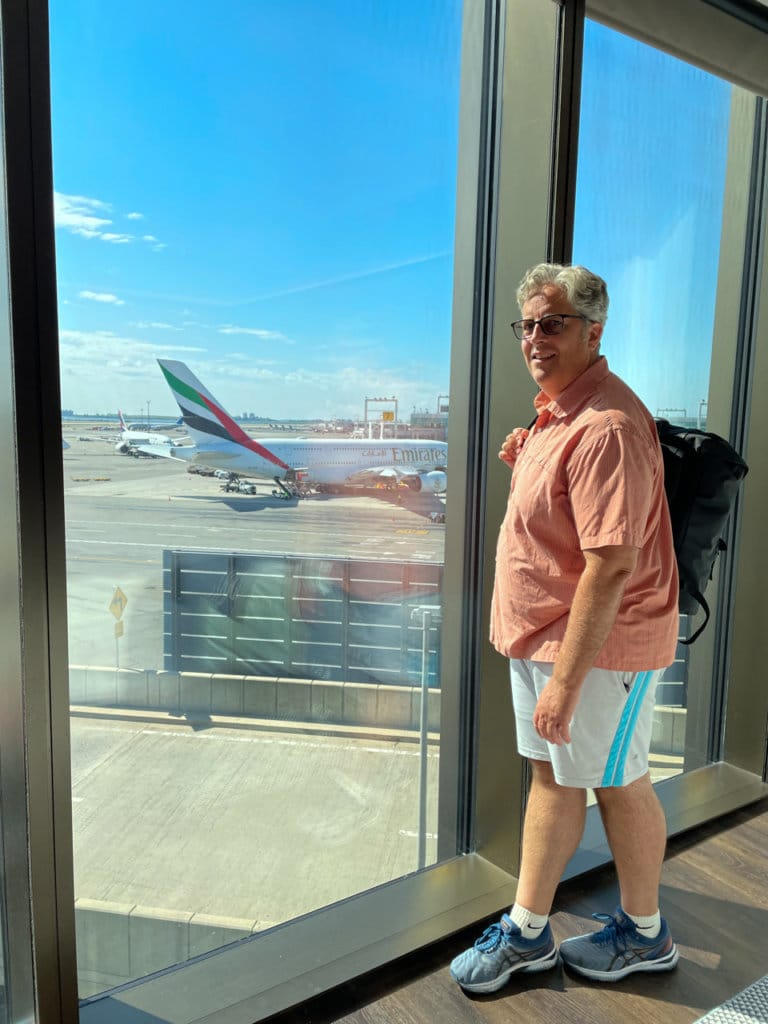 Man looking out floor-to-ceiling hotel room window onto an airport runway.